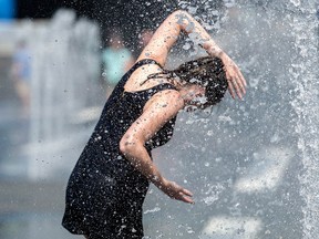 A woman cools down in a water fountain as she beats the heat in Montreal, Monday, July 2, 2018.