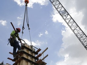 FILE- In this June 20, 2018 photo, a member of a construction team works on the site of Gables Station, a mixed use project featuring apartments, retail, a hotel and cafes, in Coral Gables, Fla. Most U.S. business economists expect corporate sales to grow over the next three months and hiring and pay to rise with them. Goods producers -- a category that includes manufacturers, farmers and construction -- are most optimistic, with 94 percent saying they expect sales to rise over the next three months.