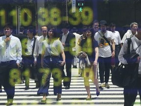 In this Wednesday, July 4, 2018, photo, people are reflected on the electronic board of a securities firm in Tokyo. Asian markets are mixed as the U.S. prepares to impose billions of dollars of tariffs on China, raising tensions between the world's two largest economies.