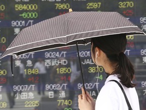 In this Wednesday, July 4, 2018, photo, a woman looks at an electronic stock board of a securities firm in Tokyo.  Asian markets are mixed as the U.S. prepares to impose billions of dollars of tariffs on China, raising tensions between the world's two largest economies.