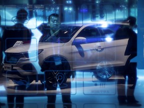 FILE - In this April 26, 2018, file photo, Chinese visitors stand near a glass panel reflecting a Chinese auto brand Lifan X70 SUV on display at the China Auto Show in Beijing. China's auto sales growth decelerated in June, adding to economic worries for Beijing amid a worsening trade battle with Washington.