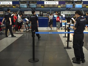 In this July 6, 2018, photo, Chinese security personnel watch as travelers check in for flights at the American Airlines check-in counters at the Beijing Capital International Airport in Beijing. China is applauding U.S. airlines for bending to its demand that they cease referring to Taiwan as its own country on their websites, as American Airlines, Delta and United are among a wave of international carriers to remove references to Taiwan on their websites ahead of a Wednesday, July 25, 2018, deadline set by Chinese authorities.
