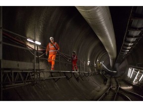 FILE  in this Wednesday April 22, 2015 file photo, workers  pass along a walkway in a Crossrail tunnel looking off in a westerly direction towards central London from the Stepney Green shaft in east London. London's new east-west railway, Crossrail, says it will miss its December opening by almost a year, with passenger services not starting until the fall of 2019. Crossrail Ltd. said in a statement Friday, Aug. 31, 2018 that the railway _ officially known as the Elizabeth Line after Queen Elizabeth II _ needs more time to finish "final infrastructure and extensive testing."