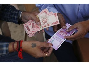 FILE - In this Nov. 18, 2016, file photo, men trade buy and sell Indian rupees at a roadside stall set up by Shri Jalaram Gaushala, a shelter for cows, in Ahmadabad, India. India's central bank says nearly all of the currency removed from circulation in a surprise 2016 attempt to root out illegal hoards of cash came back into the financial system.