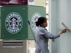 FILE - In this April 6, 2007, file photo, a woman cleans an outdoor lamp near a Starbucks coffee outlet in Beijing. Starbucks and Chinese e-commerce giant Alibaba Group announced a coffee delivery venture on Thursday that adds to growing competition in China's booming delivery industry.