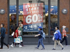 In this July 3, 2018, photo, shoppers walk past sale signs in San Francisco. On Wednesday, Aug 15, the Commerce Department releases U.S. retail sales data for July.