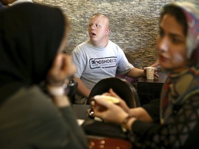In this Monday, Aug. 6, 2018, photo, cafe staff Ali Bakhti, 22, center, with down syndrome talks to his colleagues in Downtism Cafe in Tehran, Iran. The popular cafe, whose name combines "Down" with "autism," in Tehran's bustling Vanak Square is entirely run by people with Down syndrome or autism. More than just providing meaningful work, the cafe is helping break down barriers by highlighting how capable people with disabilities are.