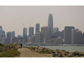 File - In this Aug. 8, 2018 file photo, a man rides a scooter on Treasure Island as the San Francisco city skyline sits in a smoky haze in the background. Alarmed by as much as $20 million in lost tourism revenue in July due to visitors' fear of wildfires, California tourism officials are teaming up with Oregon and Washington to reassure tourists they're safe to visit after deadly wildfires that have burned homes and clogged the air.
