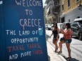 Tourists take pictures of slogans on a wall in central Athens, on August 18, 2018. - On August 20, Greece's third and final bailout officially ends after years of hugely unpopular and stinging austerity measures.