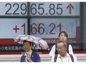 People stand in front of an electronic stock board of a securities firm in Tokyo, Tuesday, Aug. 28, 2018. Asian shares were mostly higher Tuesday after the White House said it reached a preliminary agreement with Mexico on replacing a North American free-trade deal.