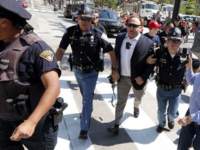 FILE - In this Tuesday, July 19, 2016 file photo, Alex Jones, center right, is escorted by police out of a crowd of protesters outside the Republican convention in Cleveland. Facebook says it has taken down four pages belonging to conspiracy theorist Alex Jones for violating its hate speech and bullying policies. The social media giant said in a statement Monday, Aug. 6, 2018 that it also blocked Jones' account for 30 days because he repeatedly posted content that broke its rules.