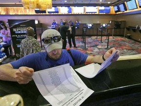 FILE - In this Aug. 3, 2018, file photo, Marvin Werkley, of Mobile, Ala., looks over the wager sheets at the IP Casino Resort & Spa in Biloxi, Miss., before making a bet. Colleges are looking for a way to get a piece of the action from legal sports wagering. Schools in states where legal wagering has started or soon will are considering joining professional sports leagues in pursuing legislation requiring sports book operators to pay them a percentage of the amount wagered on their games.