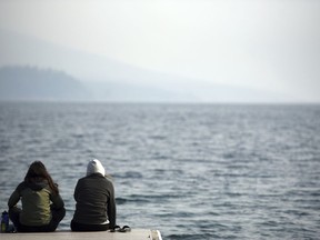 From left, Yaqmur Abay from Turkey and Anne Ruiz from Spain, two summer employees in Glacier National Park, sit on the edge of the Apgar dock with the feet in the water of Lake McDonald on Monday morning, Aug. 13, 2018. The iconic view into the park has been completely obscured and air quality has been significantly affected by multiple wildfires which are currently burning.