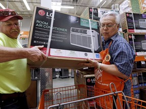 FILE - In this Aug. 1, 2017, file photo, store greeter Danny Olivar, right, lends a hand to a customer to heft an air conditioning unit from a rapidly declining stock at a Home Depot store ahead of an expected heat wave in Seattle. The Home Depot Inc. reports earnings Tuesday, Aug. 14, 2018.