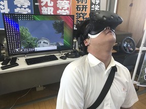 In Friday, Aug. 8, 2018, photo, Namio Matsura, 17-year-old member of the computation skill research club at the Fukuyama Technical High School, watches Hiroshima city before atomic bomb fell in virtual reality experience at the high school in Hiroshima, western Japan. Although it's impossible to relive a moment in history, a group of the students have recreated the moment an atomic bomb dropped over the city through VR to portray the livelihood of people that was taken away as a result of the bombing.