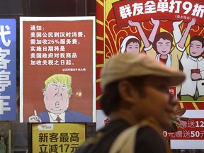 In this Monday, Aug. 13, 2018, photo, a man walks by a poster depicting a mural of U.S. President Donald Trump stating that all American costumers will be charged 25 percent more than others starting from the day president Trump started the trade war against China, on display outside a restaurant in Guangzhou in south China's Guangdong province. The recent trade war between the world's two biggest economies has forced many multinational companies to reschedule purchases and rethink where they buy materials and parts to try to dodge or blunt the effects of tit-for-tat tariffs between Washington and Beijing. (Color China Photo via AP)