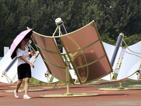 In this Thursday, Aug. 2, 2018, photo, a woman rotates a solar cooker, a device using a metal and glass vacuum tube heated by mirrors curved to capture the sun's heat, to face the sun in Dezhou in the eastern Shandong province in China. Two dozen chefs with white aprons and hats cooked soups, baked buns, potatoes, and boiled rice at a festival to demonstrate the potential of solar cookers that organizers claim can help reduce climate-changing greenhouse gas emissions.