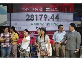 People stand in front of an electronic board showing the Hong Kong share index outside a bank in Hong Kong, Monday, Aug. 27, 2018. Asian stocks are rising as a dovish speech by U.S. Federal Reserve Chairman Jerome Powell and all-time highs on Wall Street gave markets a breather from trade tensions.