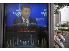 A woman sits on a scooter near a video display screen showing an image of Chinese President Xi Jinping along a street in Beijing, China, Wednesday, Aug. 22, 2018. China's increasingly image-conscious government has appointed a trusted member of the ruling Communist Party to head up its international propaganda operation.