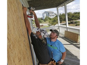 FILE - In this Wednesday, Sept. 12, 2018 file photo, Joe Gore, left, and Joshua Adcock prepare for Hurricane Florence as they board up windows on a home in Emerald Isle N.C. Before and after a hurricane, Ace is the place. And Home Depot, Lowe's, and many other hardware and building supply outlets. Not surprisingly, these companies plan for storms such as Hurricane Florence all year.