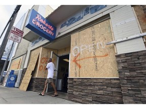 FILE- In this Tuesday, Sept. 11, 2018, file photo a man walks out of the boarded up Robert's Grocery in Wrightsville Beach, N.C., in preparation for Hurricane Florence. Though it's far from clear how much economic havoc Hurricane Florence will inflict on the southeastern coast, from South Carolina through Virginia, the damage won't be easily or quickly overcome. In those states, critically important industries like tourism and agriculture are sure to suffer. "These storms can be very disruptive to regional economies, and it takes time for them to recover," said Ryan Sweet, an economist at Moody's Analytics.