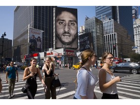 FILE - In this Sept. 6, 2018, file photo, people in New York walk past a Nike advertisement featuring former San Francisco 49ers quarterback Colin Kaepernick, known for kneeling during the national anthem to protest police brutality and racial inequality. In response to Nike's support of Kaepernick, the Rhode Island town of North Smithfield is considering asking its departments to refrain from purchasing Nike products.