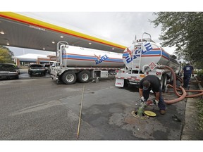 FILE- In this Sept. 17, 2018, file photo people wait in line as Travis Hall, right, and Brandon Deese, back, pump fuel from two tanker trucks at a convenience store in Wilmington, N.C.  America's rediscovered prowess in oil production is shaking up old notions about the impact of higher crude prices on the U.S. economy.