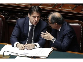 FILE  -   This Wednesday, June 6, 2018 file photo Italian premier Giuseppe Conte, left, and Italian Economy Minister Giovanni Tria talk at the Lower House, ahead of a confidence vote on the government program, in Rome, Wednesday, June 6, 2018. Italy's economy minister says that the first budget by Italy's new government will include a basic income scheme sought by one of the main governing parties, the 5-Star Movement.