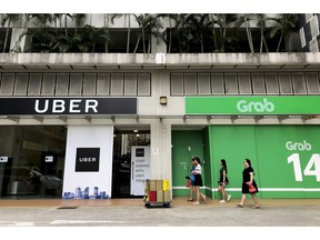 FILE - In this March 26, 2018, file photo, office workers walk past Uber and Grab offices during their lunch hour in Singapore. Singapore's competition watchdog on Monday, Sept. 24, 2018, fined ride-hailing giant Uber and its regional rival Grab 13 million Singapore dollars ($9.5 million) for a merger in Southeast Asia that the agency says has driven up fares and reduced competition in the market.