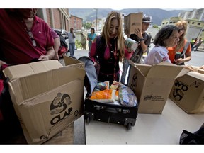 In this July 6, 2018 photo, employees of a government-supported cultural center receive boxes with subsided food distributed under a government program named "CLAP" in downtown Caracas, Venezuela. Some workers transfer the contents, cooking oil, flour, rice, canned tuna, to suitcases or backpacks for fear of becoming walking targets.