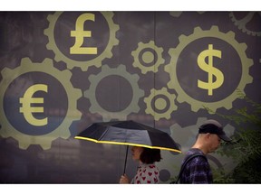 FILE - In this July 20, 2018 photo, people walk past a mural displaying world currency symbols on the outside of a bank in Beijing. Amid a worsening tariff battle, China is putting off accepting license applications from American companies in financial services and other industries until Washington makes progress toward a settlement, an official of a business group said Tuesday, Sept. 11, 2018.