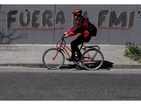 A man rides his bicycle past the Spanish graffiti message: "Get out IMF" in Buenos Aires, Argentina, Tuesday, Sept. 4, 2018. In recent weeks, the currency crisis in Argentina has intensified, forcing the government to ask for an early release of a credit line from the International Monetary Fund.