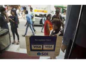 A VISA sticker is seen on the door of a shop in a market in Gauhati, India, Tuesday, Oct. 16, 2018. A customer uses a bank card to buy clothes inside a shop in Gauhati, India, Tuesday, Oct. 16, 2018. Global credit card and payments companies like American Express, Visa and MasterCard are facing a challenge in meeting a requirement to store transaction data for all Indian customers within the country.