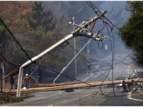 FILE - In this Tuesday, Oct. 10, 2017 file photo, people walk past a fallen transformer and downed power lines in Santa Rosa, Calif. California fire officials say sagging Pacific Gas and Electric power lines that made contact ignited a blaze last year in California that killed four people and injured a firefighter. The California Department of Forestry and Fire Protection said Tuesday, Oct. 9, 2018, that strong winds caused the lines to come into contact and send molten material onto dry vegetation in Yuba County. It was one of several wildfires that swept through Northern California that month, killing 44 people.