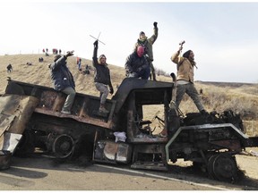 FILE - In this Nov. 21, 2016, file photo, protesters against the Dakota Access oil pipeline stand on a burned-out truck near Cannon Ball, N.D. In a lawsuit filed, Friday, Oct. 19, 2018, two members of the Standing Rock Sioux tribe and a reservation priest are suing over a five-month shutdown of a North Dakota highway during protests against oil pipeline, saying the closure violated their and others' constitutional rights.