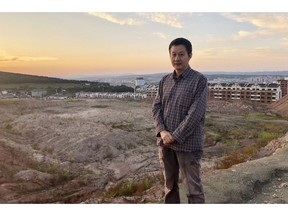In this Sept. 12, 2018, photo, paleontologist Xu Xing stands in front of a dig site in Yanji, China. The excavation was begun after construction crews erecting new apartment buildings, visible in the background, accidentally uncovered dinosaur bones and other fossils, dating back 100 million years.