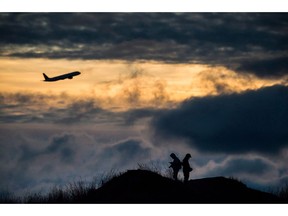 An Air Canada plane takes off as Andrew Yang, left, and Kevin Jiang take photographs of planes taking off and landing at Vancouver International Airport at sunset, in Richmond, B.C., on Sunday, December 31, 2017. Canadian airlines are urging Ottawa to delay the Jan. 1 start date of the carbon tax, which they warn will boost airfares and push passengers to airports across the border.