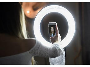 In this Feb. 28, 2018 photo, Matty Nev Luby holds up her phone in front of a ring light she uses to lip-sync with the smartphone app Musical.ly, in Wethersfield, Conn. Teens and young adults say cyberbullying is a serious problem for people their age, but most don't think they'll be the ones targeted for digital abuse. The high school gymnast's popularity on the lip-syncing app Musical.ly, which merged this summer into the Chinese video-sharing app TikTok, helped win her some modeling contracts. Luby said she's learned to navigate Instagram and other social media apps by brushing aside the anonymous bullies.