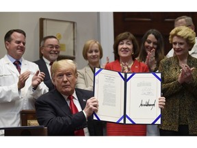 President Donald Trump holds up the 'Patient Right to Know Drug Prices Act' after signing it and the 'Know the Lowest Price Act of 2018,' during a ceremony in the Roosevelt Room of the White House in Washington, Wednesday, Oct. 10, 2018. These bills, which were sponsored by Sen. Susan Collins, R-Maine, in red, and Sen. Debbie Stabenow, D-Mich., right, help protect Medicare patients and those with private insurance from overpaying for prescription drugs by outlawing pharmacy "gag clauses."