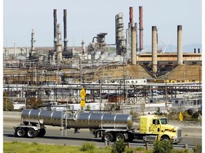 FILE - This March 9, 2010, file photo shows a tanker truck passing the Chevron oil refinery in Richmond, Calif. Federal officials say Chevron Corp. has agreed to pay a nearly $3 million fine and spend $160 million on environmental improvements and upgrading oil refineries to resolve allegations the company violated pollution laws. The U.S. Department of Justice announced the agreement Wednesday, Oct. 24, 2018.