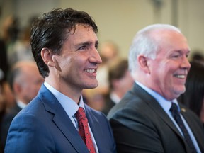 Prime Minister Justin Trudeau, left, and B.C. Premier John Horgan smile while sitting together during an LNG Canada news conference in Vancouver.