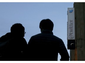 FILE- In this Oct. 26, 2016, file photo two men wait to cross the street under a sign at Twitter headquarters in San Francisco. Twitter says it is releasing all of the accounts and posts related to "information operations" it has found on its service since 2016 when it and other social media companies were first found to have been used by foreign agents to meddle with U.S. elections.