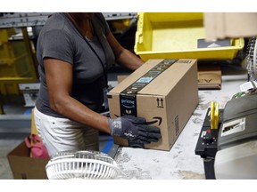 FILE- In this Aug. 3, 2017, file photo, Myrtice Harris applies tape to a package before shipment at an Amazon fulfillment center in Baltimore. Amazon's announced Tuesday, Oct. 2, 2018, that it would raise its hourly minimum wage to $15. Those who already made $15 will get an extra dollar an hour when the change is made next month, but they will also lose two benefits they relied on: monthly bonuses that could top hundreds of dollars and a chance to own Amazon's sky-rocketing stock, currently worth nearly $2,000.