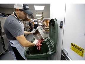 In this Aug. 22, 2018, photo, Konrad Navarrete, part of the kitchen crew at Dos Toros restaurant, dumps leftover meat into the organics processing bin inside the kitchen of the restaurant in New York. New York City began requiring chain restaurants to separate their food waste from other trash this year.