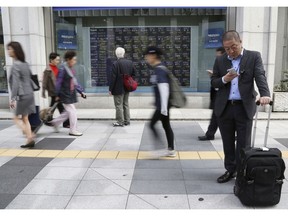 In this Oct. 10, 2018, photo, people walk by an electronic stock board of a securities firm in Tokyo. Asian stock markets sank Friday, Oct. 19, 2018, after Wall Street declined on losses for tech and industrial stocks and Chinese economic growth slowed.