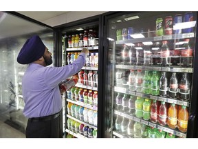 In this Monday, Oct. 1, 2018, shop owner Prem Singh reaches into a drink cooler at his convenience store in Kent, Wash. In the wake of Seattle's new tax on sugary beverages, a group backed by millions of dollars from the soda industry will ask voters in November whether to prevent other cities and counties in Washington from following suit. Under Initiative 1634, local governments would no longer be able to impose their own taxes on sodas, other sugary beverages and on food items.