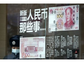 FILE - In this file photo taken Sunday, Jan. 1, 2017, a security guard wearing a protection mask against air pollution takes a rest near a bank window panel displaying the security markers on the latest Yuan note in Beijing. China's government on Tuesday, Oct. 9, 2018 promised not to weaken its currency to boost exports and rejected U.S. concern about the sagging yuan as groundless and irresponsible.