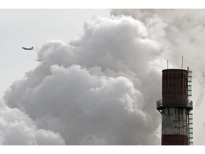 FILE - In this file photo taken Tuesday, Feb. 28, 2017, a passenger airliner flies past steam and white smoke emitted from China Huaneng Group's Beijing power plant that was the last coal-fired plant to shut down on March 18, 2017 as the Chinese capital convert to clean energy like thermal power.