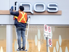 A worker removes IQOS store signs from its location on Yonge Street in Toronto.