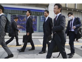 People walk by an electronic stock board of a securities firm in Tokyo, Wednesday, Nov. 14, 2018.  Asian shares were mostly lower Wednesday, after the steepest drop in oil prices in more than three years put investors in a selling mood on Wall Street.